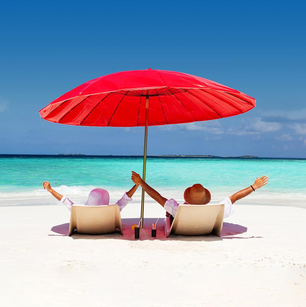 couple seated beneath a red beach umbrella on the beach overlooking the ocean