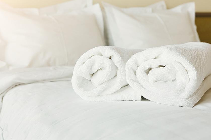 White rolled bath towels and crisp white hotel linens await hotel guests on bed